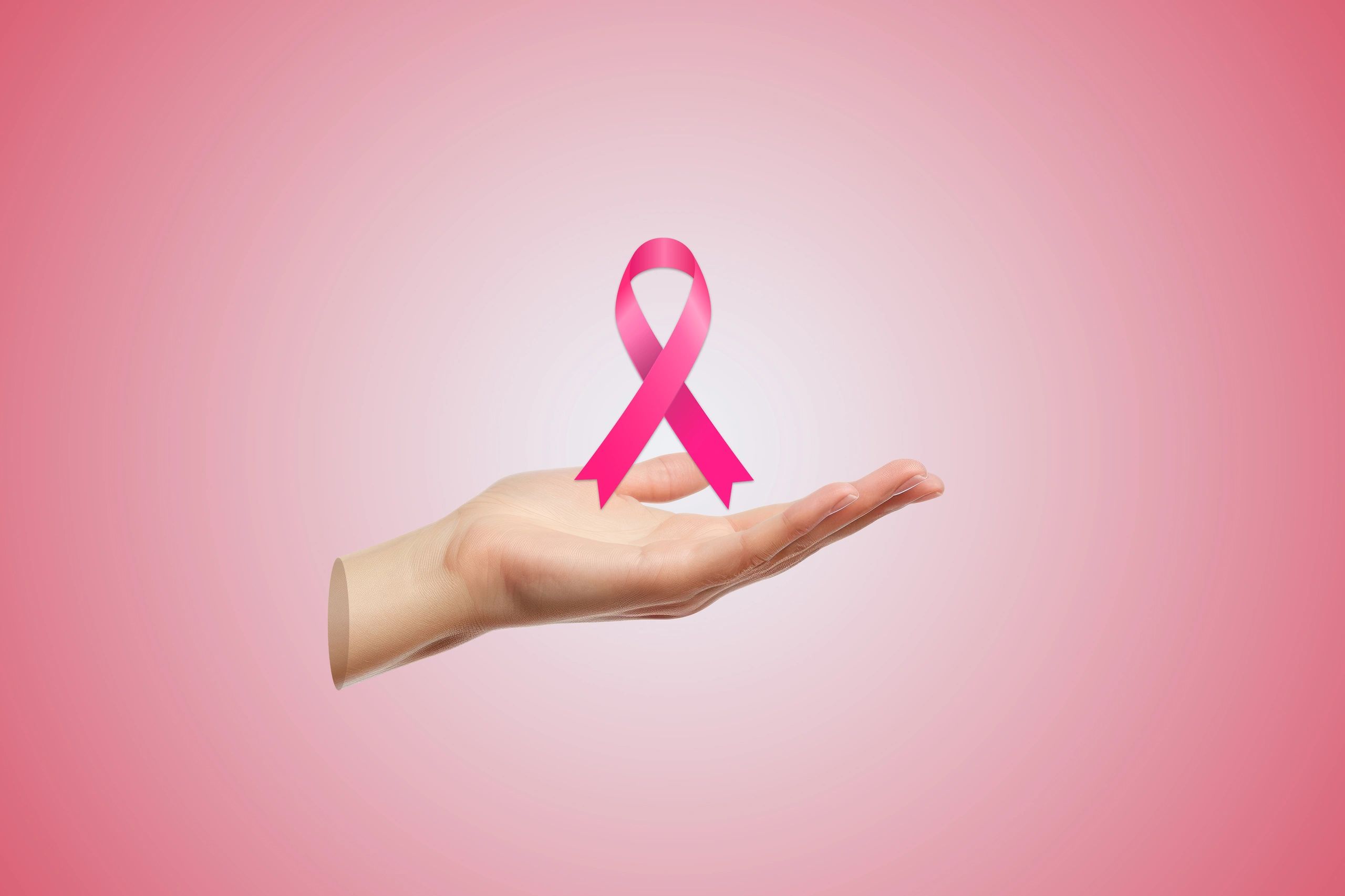 Hand holding a pink ribbon for breast cancer awareness